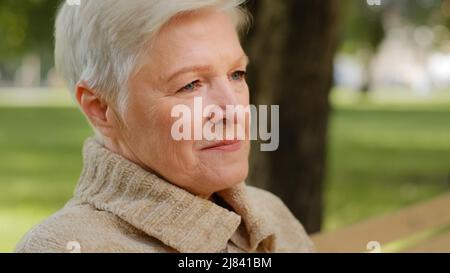 Primo piano ritratto di felice età bella donna guardando la macchina fotografica rilassante posa all'aperto in clima fresco, sorridente donna anziana donna sensazione di signora Foto Stock