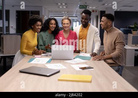 Sorridendo le donne d'affari biraciali e gli uomini d'affari che discutono sopra il laptop durante la riunione sul posto di lavoro Foto Stock