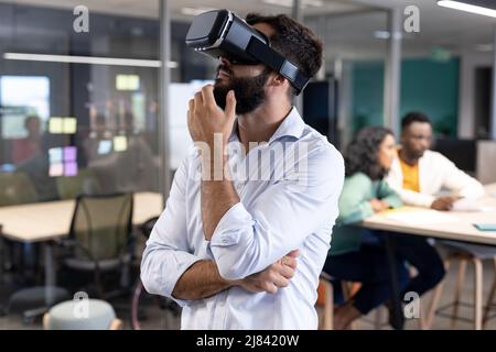 Uomo d'affari caucasico con simulatore di realtà virtuale che contempla nel luogo di lavoro moderno Foto Stock