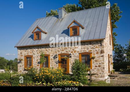 Replica del vecchio 1700s francese regime cottage stile fieldstone casa con tetto di lamiera grigio in estate. Foto Stock