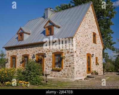 Replica del vecchio 1700s francese regime cottage stile fieldstone casa con tetto di lamiera grigio in estate. Foto Stock