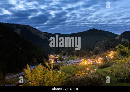 Luci da piccolo villaggio in montagne scure sotto le nuvole dopo il tramonto Foto Stock