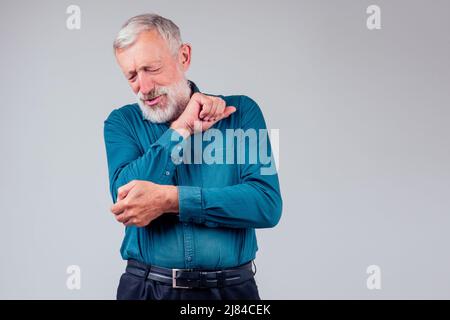 vecchio uomo in camicia verde con occhi chiusi che tiene il gomito in dolore nello studio sfondo bianco Foto Stock