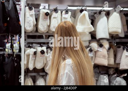 Donna bionda che guarda i cappelli a maglia e i guanti appesi nel deposito Foto Stock
