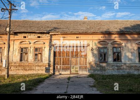 Foto di una fattoria abbandonata in Vojvodina, in Serbia, con la facciata della sua casa principale gravemente danneggiata e decadente. Foto Stock