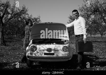 Giovane coppia caricando le valigie su un'auto d'epoca per la partenza di una vacanza. Foto Stock