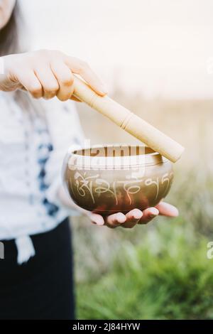 Donna all'aperto che tiene e gioca una ciotola di canto tibetano con un bastone di legno. Messa a fuoco selettiva. Foto Stock