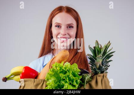 bella donna zenzero rosso con sacco di cotone ecologico pieno di prodotti: banana, ananas, verdure Foto Stock