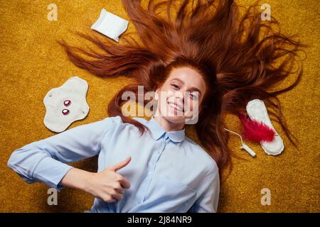 zenzero rosso capelli lunghi donna sdraiati a terra con eco-friendly guarnizioni organiche in bio-cotone e monouso tampon.making scelta Foto Stock