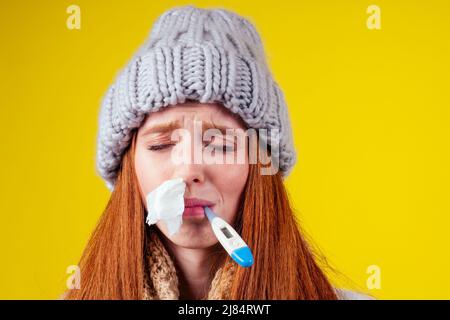 malbene rosso zenzero donna naso runny indossare maglione a maglia e sciarpa con molte pillole in mano in studio sfondo giallo Foto Stock