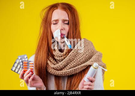 malbene rosso zenzero donna naso runny indossare maglione a maglia e sciarpa con molte pillole in mano in studio sfondo giallo Foto Stock