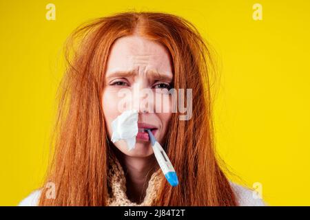 malbene rosso zenzero donna naso runny indossare maglione a maglia e sciarpa con molte pillole in mano in studio sfondo giallo Foto Stock