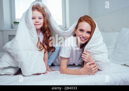 due ragazze allegre di zenzero rosso che giocano a nascondino e cercano sotto coperta bianca Foto Stock