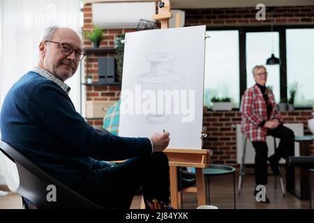 Ritratto di studente senior di classe in piedi di fronte su tela di pittura disegno vaso artistico utilizzando tecnica di schizzo durante la lezione d'arte in studio di creatività. Il pittore anziano havnig hobby creativo Foto Stock