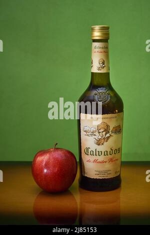 Bottiglia di brandy calvados e una mela su un tavolo di legno su sfondo verde. Maitre Pierre calvados, prodotto della società francese Slaur Sardet Foto Stock