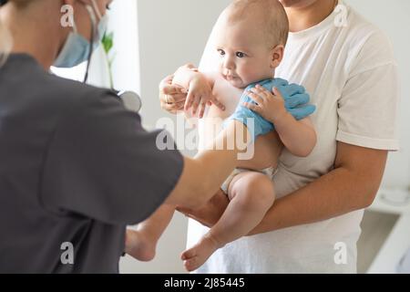 Femmina medico che esamina la bambina piccola sorridente, tenuta dalla madre Foto Stock