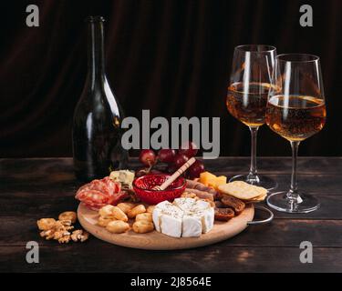 Piatto di salumi e formaggi. Salsiccia e formaggio tagliati con frutta, biscotti e salsa con due bicchieri di porto bianco e una bottiglia. Foto Stock