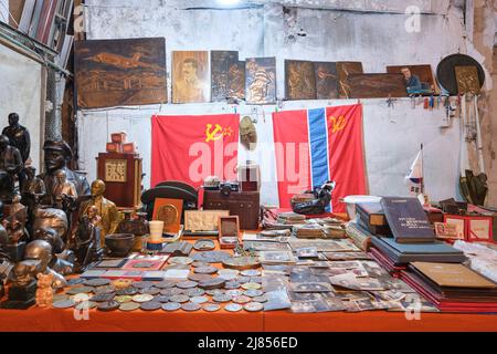 Vecchie bandiere russe dietro ad un tavolo pieno di vecchie monete, busti di leader sovietici. Presso il mercato di Yangiobod Bozor a Tashkent, Uzbekistan. Foto Stock