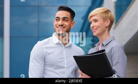 Coppia multirazziale due colleghi d'affari due architetti uomo e donna caucasica tenuta cartella in mano in piedi all'aperto parlare di nuovo Foto Stock