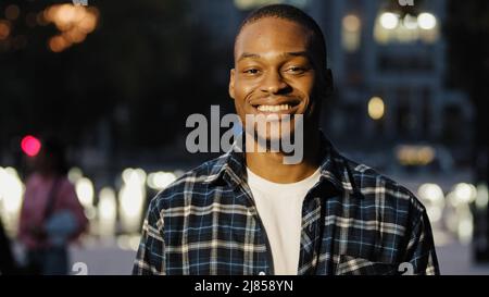 Ritratto Happy african american 20s millennial soddisfatto uomo ragazzo si erge in città in sfondo sera guardando la macchina fotografica sorridente toothy dentale posa Foto Stock