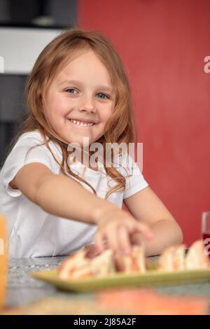 Ragazza sorridente carina con sushi su sfondo bianco. Bambina che mangia sushi e panini - concetto commerciale. Foto Stock