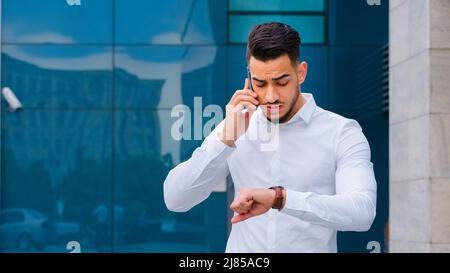 Ritratto riuscito grave arabo ispanico business man spaniard capo capo capo indossa bianco formale camicia stand esterni parla cellulare Foto Stock