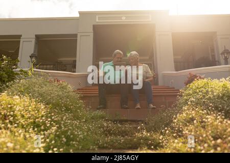 Vista ad angolo basso dell'anziano biraciale che mostra tablet digitale a moglie mentre si siede sui gradini Foto Stock