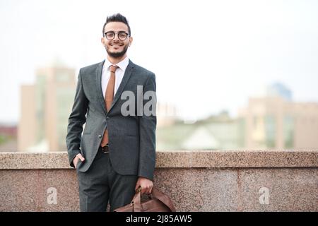 Ritratto di bell'uomo d'affari medio-orientale con barba in piedi con valigetta sul terrapieno Foto Stock