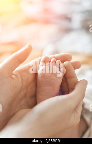 Piedi del bambino. La mamma tiene con tenerezza e amore nelle mani le piccole gambe di un neonato. Nuova vita, protezione dei genitori, cura, amore, salute dei bambini e dei bambini. Foto di alta qualità Foto Stock