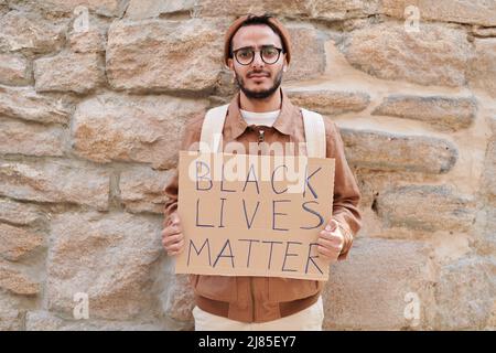 Ritratto di giovane medio-orientale sconvolto in giacca mostrando nero banner materia viva mentre si chiede di sostegno in protesta Foto Stock