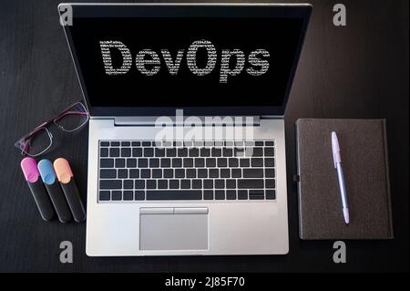 Vista dall'alto del notebook con testo DevOps. Iscrizione DevOps sullo schermo del notebook. DevOps combina lo sviluppo del software e le operazioni IT. Foto Stock
