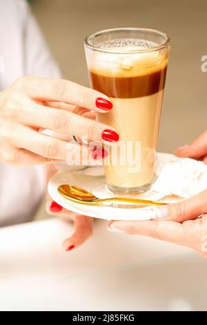 Barista che serve caffè latte in tazza di vetro per un cliente, mani ravvicinate Foto Stock