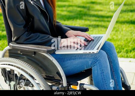 redhead zenzero freelancer donna seduta in sedia a rotelle e di lavoro da computer portatile nel parco estivo Foto Stock