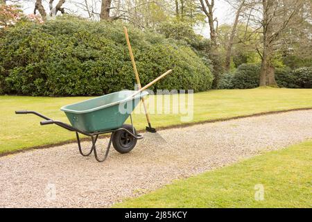 ralla per giardinieri in verde e attrezzi su un percorso di ghiaia e un prato ben tenuto Foto Stock