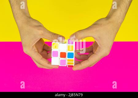 Mani che giocano con cubo colorato con sfondo rosa e giallo, intelligenza e gioco di cervello, vista dall'alto, vista dall'alto di un cubo Foto Stock