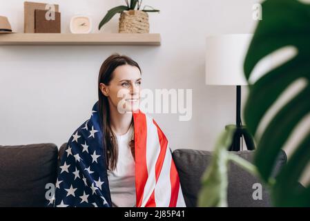 Vista laterale di bella bella signora coperta grande bandiera americana degli stati uniti che celebra nazionale tradizionale vacanza, attraente sorridente giovane donna caucasica si Foto Stock