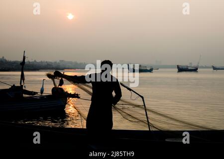 Silhouette di pescatore in piedi in barca con rete da pesca, Tangassery, Kerala, India. Foto Stock