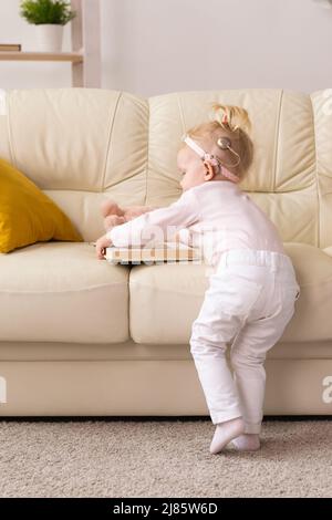 Bambino divertente con impianto cocleare seduta a casa e mangiare. Ascolta il concetto di tecnologia innovativa di aiuto e medicina Foto Stock