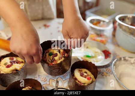 Una cuoca donna stende l'impasto con frutta candita in stampi di carta per cuocere le torte di Pasqua. Tradizioni e ricette familiari. Piccola impresa familiare e. Foto Stock