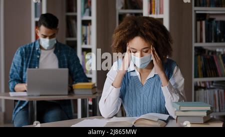 Due studenti in maschera protettiva seduta in aula alla biblioteca universitaria facendo i compiti di preparazione esame giovane ragazza alla ricerca di informazioni nel libro Foto Stock