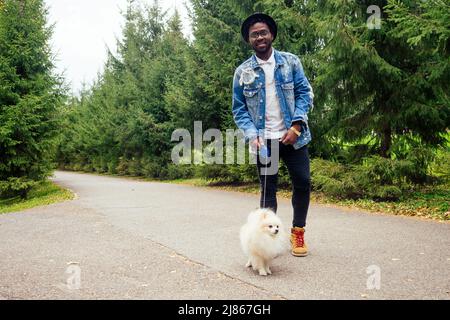 afro uomo abbracciando il suo soffice spitz nel parco Foto Stock