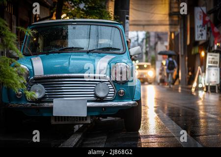 Piccola auto blu e bianca parcheggiata nella strada piovosa in Giappone Foto Stock