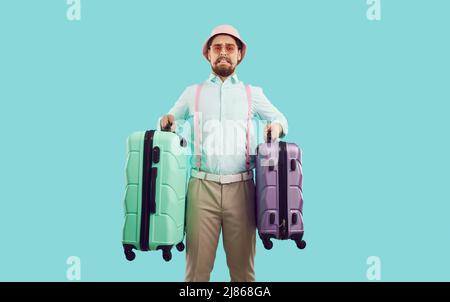 Imbarazzato ragazzo turistico che tiene due valigie di viaggio troppo pesanti isolato su sfondo azzurro chiaro. Foto Stock