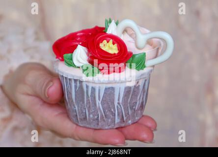 Splendido bouquet di fiori glassato con cupcake al cioccolato bianco a forma di cuore in mano della donna Foto Stock