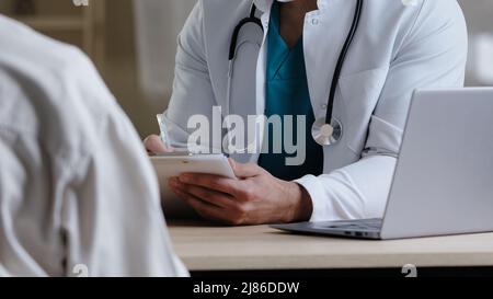 Primo piano vista maschio sconosciuto medico terapista uomo in uniforme medica bianca sedersi alla scrivania consultare i reclami del paziente dare consiglio al collega medico intern Foto Stock