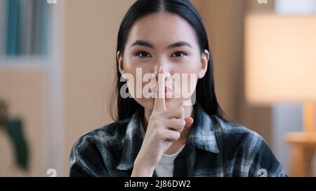 Ritratto asiatico etnia coreana punto donna con dito vicino bocca cinese giapponese ragazza fa hush tranquillo gesto mostrando segno segreto chiede silenzio Foto Stock