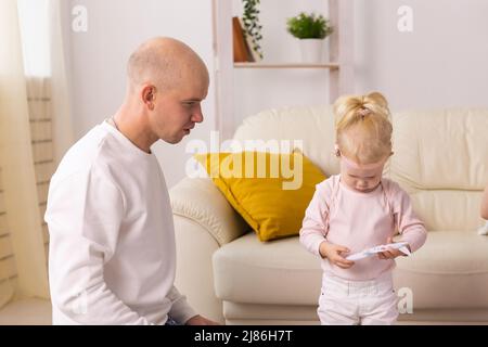 Bambino con impianti cocleari che gioca con suo padre a casa. Sordità e tecnologia medica concetto Foto Stock