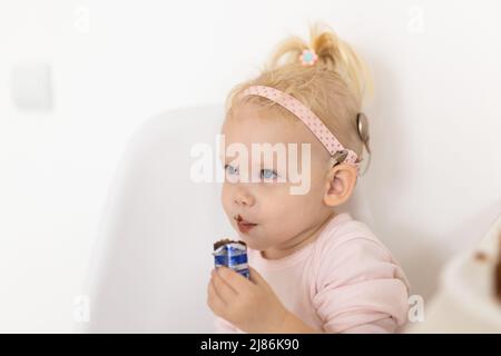 Bambino divertente con impianto cocleare seduta a casa e mangiare. Ascolta il concetto di tecnologia innovativa di aiuto e medicina Foto Stock