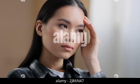 Ritratto in casa ragazza asiatica millennial donna pensieri difficili pensare risolve il problema rubi fronte con mano sente mal di testa soffre di emicrania Foto Stock