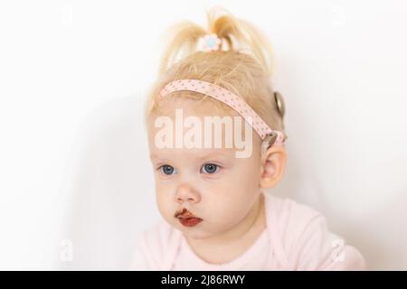 Bambino divertente con impianto cocleare seduta a casa e mangiare. Ascolta il concetto di tecnologia innovativa di aiuto e medicina Foto Stock